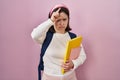 Woman with down syndrome wearing student backpack and holding books making fun of people with fingers on forehead doing loser