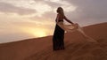 Woman in dress with a silk scarf, view of desert sand in sunset light. Landscape Royalty Free Stock Photo