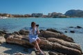 Woman in a dress sitting on the rocks on the beach and taking pictures with a SLR camera. Sea and mountains in the background Royalty Free Stock Photo