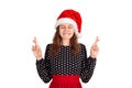 Woman in dress smiling broadly, closing eyes and raising crossed fingers while praying and hoping. emotional girl in santa claus c