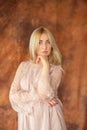 Woman in a dress in a studio. Young blond woman in a beige dress flirts with a camera squatting