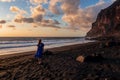 Woman in dress walking barefoot on volcanic sand beach Playa del Ingles during sunset in Valle Gran Rey on La Gomera,