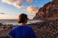 Woman in dress walking barefoot on volcanic sand beach Playa del Ingles during sunset in Valle Gran Rey on La Gomera,