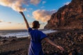 Woman in dress walking barefoot on volcanic sand beach Playa del Ingles during sunset in Valle Gran Rey on La Gomera,