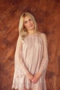 Woman in a dress in a studio. Young blond woman in a beige dress flirts with a camera squatting