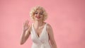 A woman dressed as Marilyn Monroe waves her hand in greeting. A woman in a white dress and white wig with red lipstick Royalty Free Stock Photo