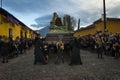 Woman dressed in black carrying a giant float in a street of the old city of Antigua during a procession of the Holy Week with a v