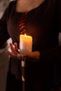 A woman dressed in a medieval dress holds a burning white candle in her hand. Mystery witch Royalty Free Stock Photo