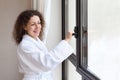 Woman dressed in white bathrobe opens window