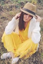 Woman dressed in yellow dress, white jersey and hat sitting on autumn field. Royalty Free Stock Photo