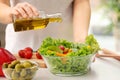 Woman dressing fresh vegetable salad with olive oil in kitchen Royalty Free Stock Photo