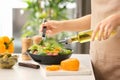 Woman dressing fresh vegetable salad with olive oil in kitchen Royalty Free Stock Photo