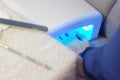 Woman dries her nails with gel polish base coat in UV lamp, hands closeup.