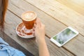 A woman drinking coffee and using phone on wood table