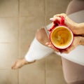 Woman drinking coffee. Young female manicured hands holding cup of hot coffee with fresh foam on floor background.