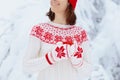 Woman drinking hot chocolate in Christmas morning in snowy garden. Girl in knitted Nordic sweater, hat and mittens holding cup Royalty Free Stock Photo