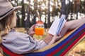 Woman drinking orange smoothie while resting and reading book in hammock Royalty Free Stock Photo