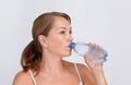 Woman drinking pure water from plastic bottle on white background