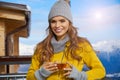 Woman drinking warm tea in the rustick wooden terrace on mountain, alpine view, snow on hills