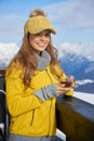 Woman drinking warm tea in the rustick wooden terrace on mountain, alpine view, snow on hills