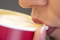 A woman drinks coffee with milk foam from a red paper Cup, selective focus, close-up. Royalty Free Stock Photo