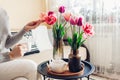 Woman drinks tea enjoying fresh tulips flowers in vase on coffee table. Interior and spring home decor. Royalty Free Stock Photo
