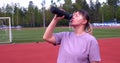 A woman drinks water from a bottle after an active workout in the park in summer. Actively doing sports on a hot day, a Royalty Free Stock Photo