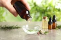 Woman dripping natural tea tree oil in bowl against blurred background