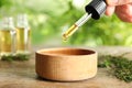 Woman dripping natural tea tree oil in bowl on table