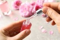 Woman dripping rose essential oil into bottle over table