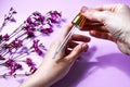 Woman dripping rose essential oil on hand against blurred flowers on pink background, closeup, white spa towel, beauty treatment, Royalty Free Stock Photo