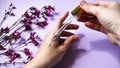 Woman dripping rose essential oil on hand against blurred flowers on pink background, closeup, white spa towel, beauty treatment, Royalty Free Stock Photo