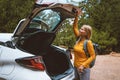 Woman driver traveling by car. Girl opens trunk. Road trip with rental auto summer vacations