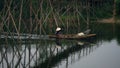 Woman drives a boat with fishing gear under a bamboo bridge