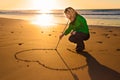 Woman drowing a heart shape in the sand.