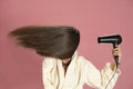 Woman drying her long hair with electric fan on a pink background Royalty Free Stock Photo