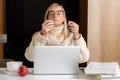 Woman in earphones using cellphone while working with laptop at home kitchen Royalty Free Stock Photo