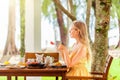 Woman eating breakfast, drinking coffee in cafe in tropical resort