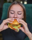 Woman eating burger and fries smiling. Beautiful caucasian female model eating a hamburger with hands Royalty Free Stock Photo