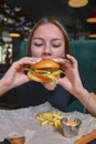 Woman eating burger and fries smiling. Beautiful caucasian female model eating a hamburger with hands Royalty Free Stock Photo