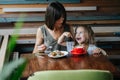 Woman eating cake in a cafe with her daughter helping her Royalty Free Stock Photo