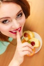 Woman eating cake showing quiet sign. Gluttony.