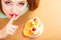 Woman eating cake showing quiet sign. Gluttony.