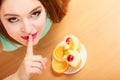 Woman eating cake showing quiet sign. Gluttony.