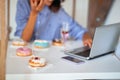 A woman is eating delicious donuts while sitting and using a laptop in a pastry shop. Pastry shop, dessert, sweet Royalty Free Stock Photo