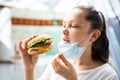 Woman Eating Fastfood Burger In Face Mask