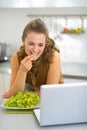 Woman eating grape in kitchen and using laptop Royalty Free Stock Photo
