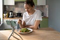 Woman eating pasta with vegetarian pesto sauce, watching movie on smart phone on tripod at home. Royalty Free Stock Photo