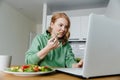 Woman eating salad and working using laptop in her kitchen Royalty Free Stock Photo