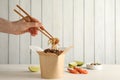 Woman eating seafood wok noodles with chopsticks from box at white wooden table, closeup. Space for text Royalty Free Stock Photo